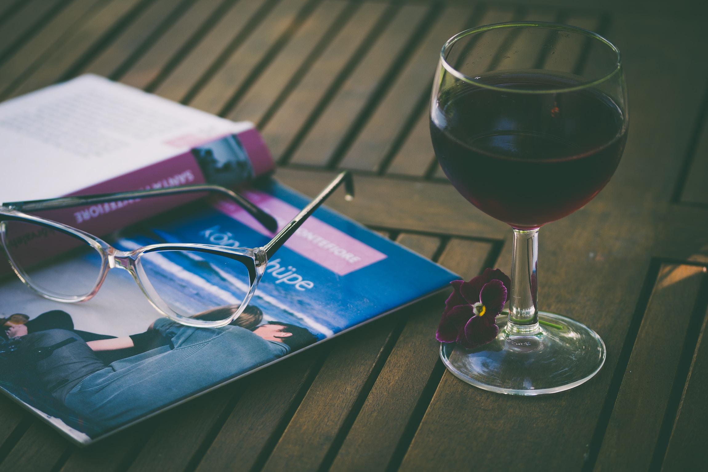 The best wine courses you can attend to study wine. In the image, you can see a book and a pair of glasses, with a glass of red wine, on a brown desk.