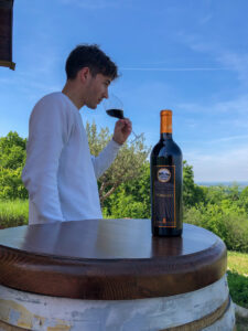 Ragazzo che degusta un vino rosso corposo, di grande struttura, Il Poggio di Salsomaggiore Terme, il tutto immerso nel panorama verdeggiante delle colline di Cangelasio